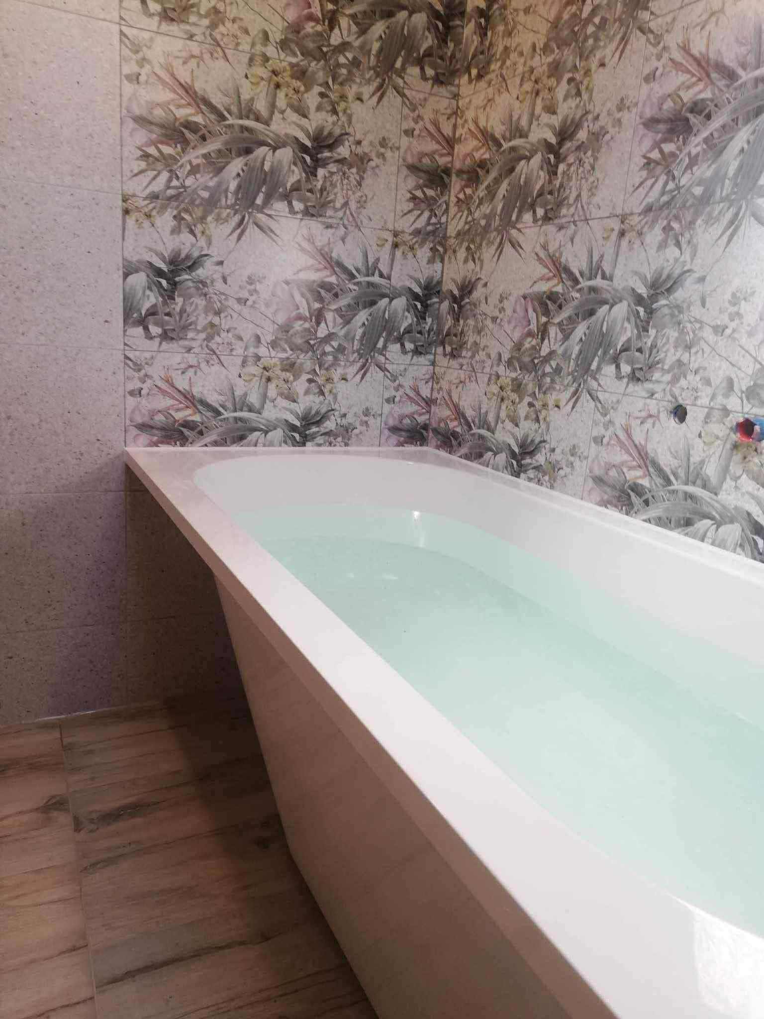 Įrengta vonia prie gėlių rašto dekoro plytelėmis išklijuotos sienos